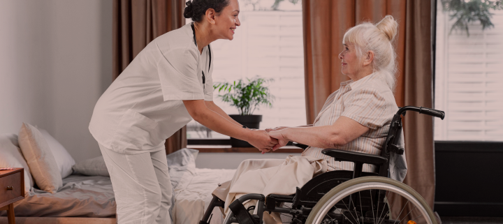 Cuidadora segurando mão de idosa que está em cadeira de rodas